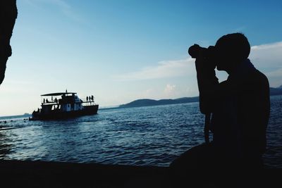 Silhouette man photographing boat in sea against sky