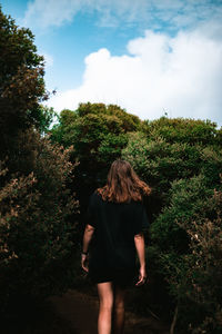 Rear view of woman standing by plants against trees