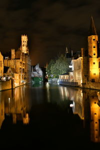 Illuminated buildings by river against sky in city at night