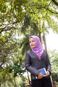 Young woman holding digital tablet while walking at park