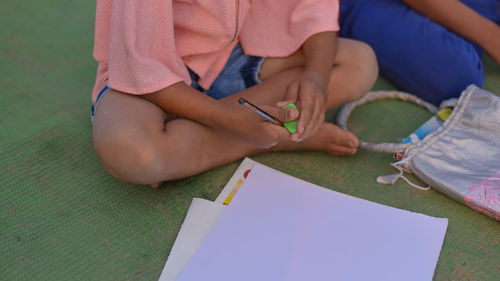 Low section of girl holding eraser and pencil while sitting on mat