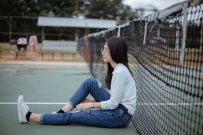 Young woman sitting against tennis net at court