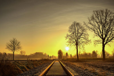 Railroad tracks amidst trees against sky during sunset