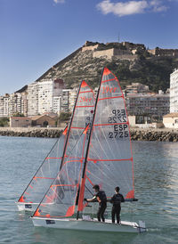 People standing on sailboat by sea against sky in city