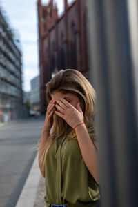 Tired woman with head in hands standing on footpath in city