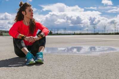 Young woman looking away while sitting on road against sky