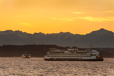 Ferry boats sailing in sea against orange sky