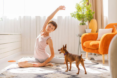 Cute woman practicing yoga with dog breed pygmy pinscher, enjoy and relax
