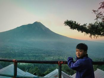 Boy standing on railing against mountains