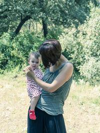 Mother carrying toddler daughter at park