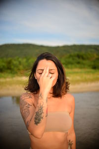 Young woman looking away while standing against lake