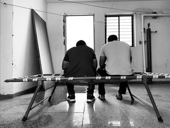 Rear view of men sitting on wall