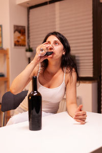 Portrait of young woman drinking glass on table