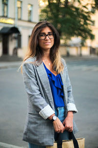 Portrait of smiling young woman standing on footpath in city