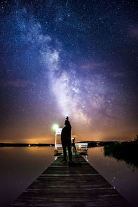 Silhouette man standing on pier against sky at night