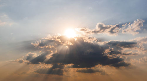 Low angle view of sunlight streaming through clouds