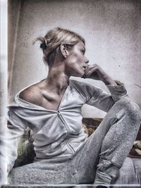 Young woman looking away while sitting on wall