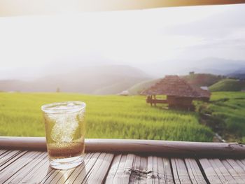 Glass on table by field against sky