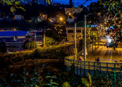 Illuminated city street by buildings at dusk