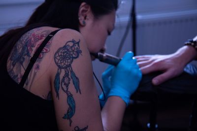 Woman tattooing on man hand at studio