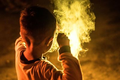 Close-up of young man holding cigarette at night