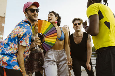 Non-binary person holding hand fan and dancing with multiracial friends in city