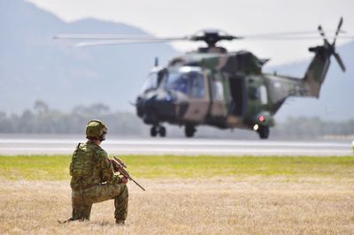 Rear view of army soldier with gun kneeling on field