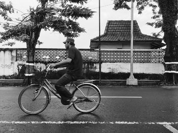 Side view of man cycling on road by house