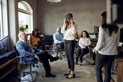 Male and female colleagues watching businesswoman wearing vr simulator at office