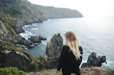 Rear view of woman standing on rock by sea against sky