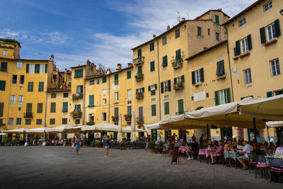 People on street by buildings in city against sky