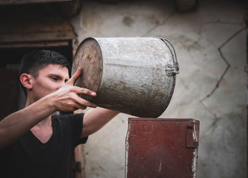 A young guy pours wheat from a bucket into a crusher.