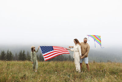 People with umbrella standing on field against sky