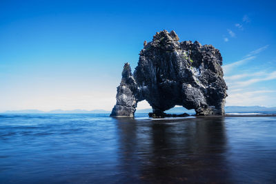 View of rock formation in sea against blue sky