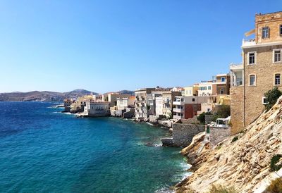 Buildings by sea against clear blue sky