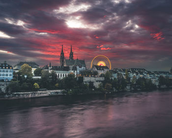 Illuminated buildings in city against cloudy sky at sunset