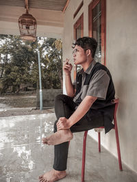 Full length of young man smoking while sitting on chair