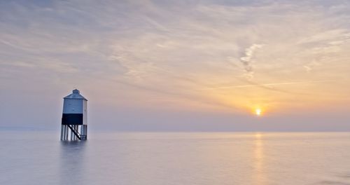 Scenic view of lighthouse in sea against sky during sunset