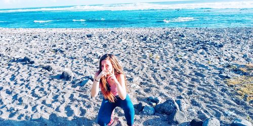Portrait of girl gesturing while crouching at beach
