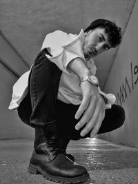 Low angle portrait of young man crouching against wall