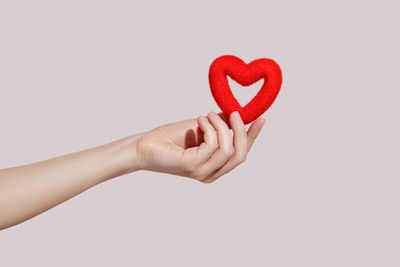 Cropped hand of person holding red heart shape against white background