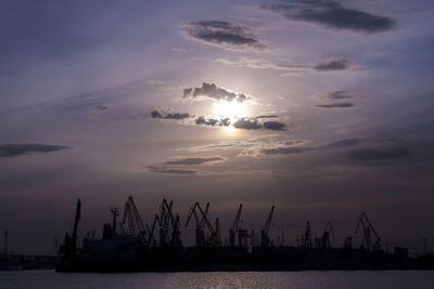 Cranes at commercial dock against sky during sunset