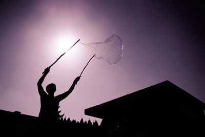 Low angle view of silhouette man holding purple against sky during sunset