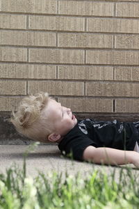 Fallen boy crying on footpath against brick wall