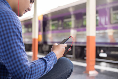 Side view of man using mobile phone while sitting at railroad station platform