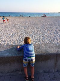 Rear view of boy standing at beach against sky