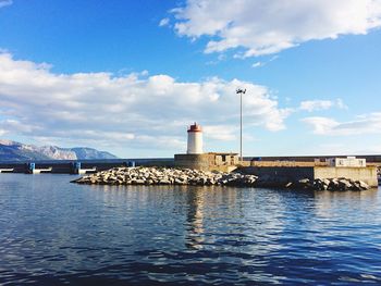 Lighthouse at harbor against cloudy sky