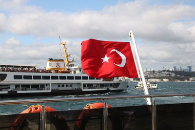 Red flag on boat in city against sky