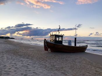 Sailboats moored on beach against sky during sunset