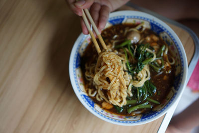 Midsection of person holding noodles in bowl on table